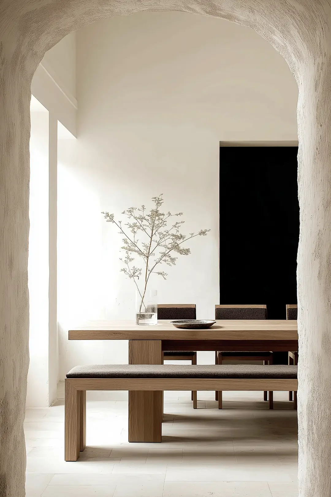 Minimalist dining room in Dubai by Studio Sakaia with oak table, textured archway and sculptural branch arrangement.