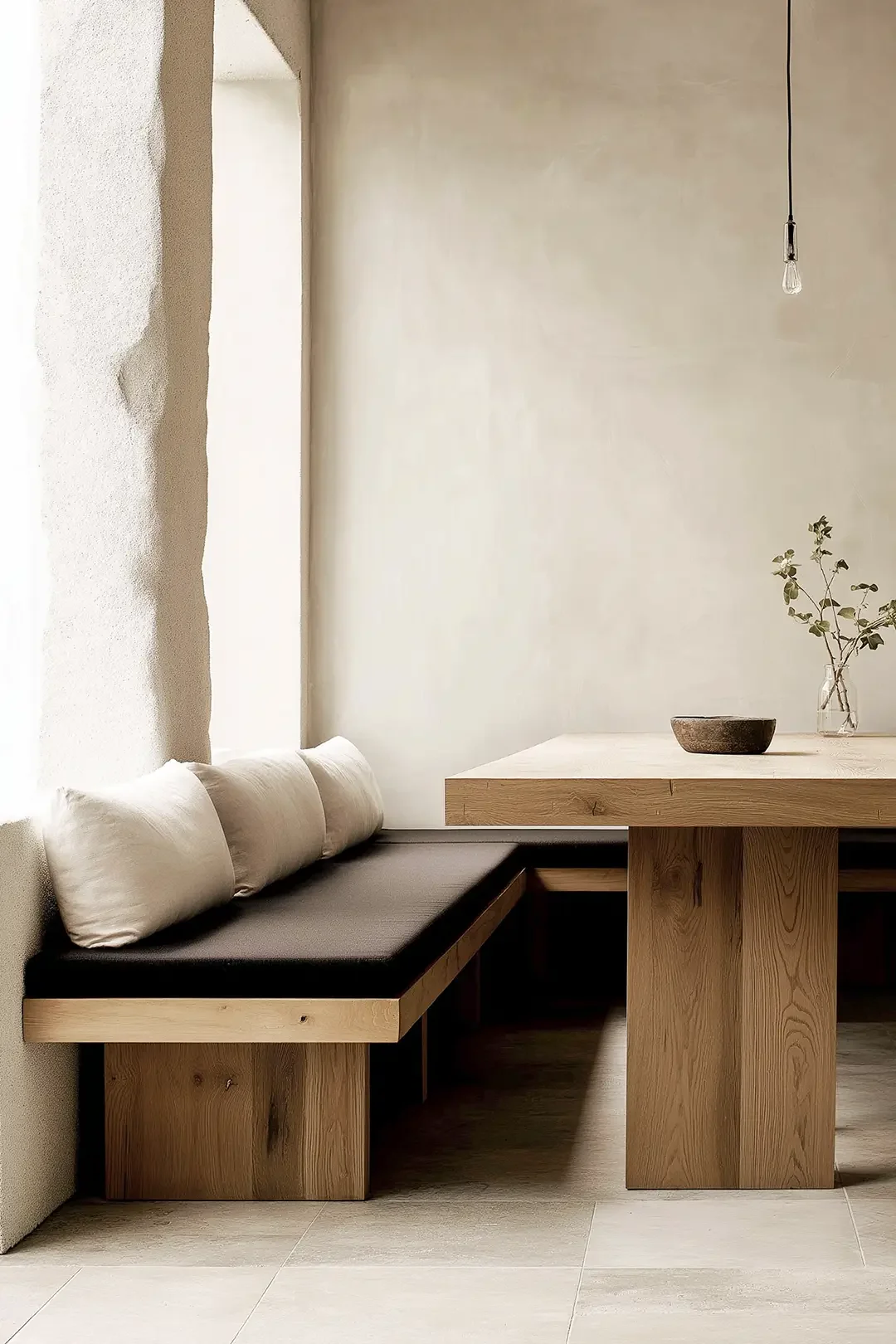 Modern dining nook with built-in oak bench, black cushions, neutral palette and ambient lighting by Studio Sakaia.