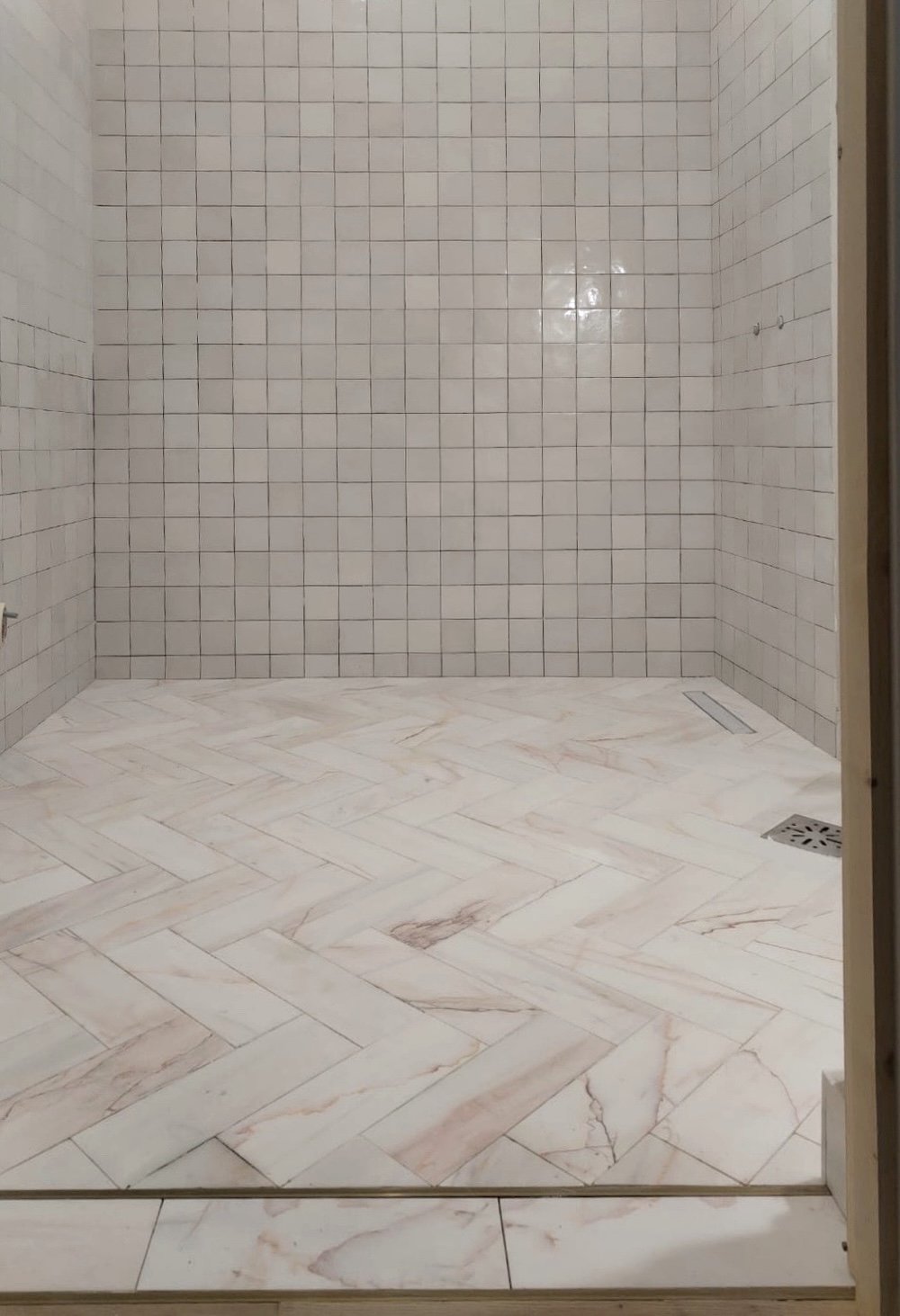 Studio Sakaia bathroom with marble herringbone floor and Moroccan zellige tile shower walls, blending soft blush veining with artisanal texture.