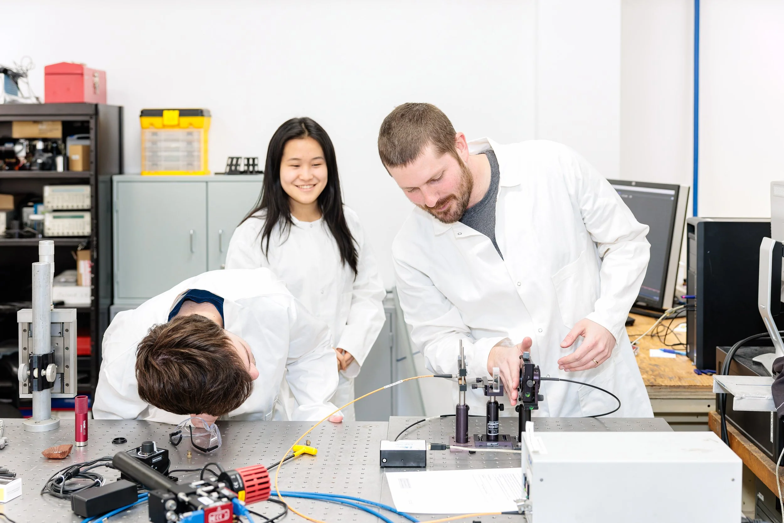 Four people in lab coats work and observe scientific equipment and experiments in a laboratory.
