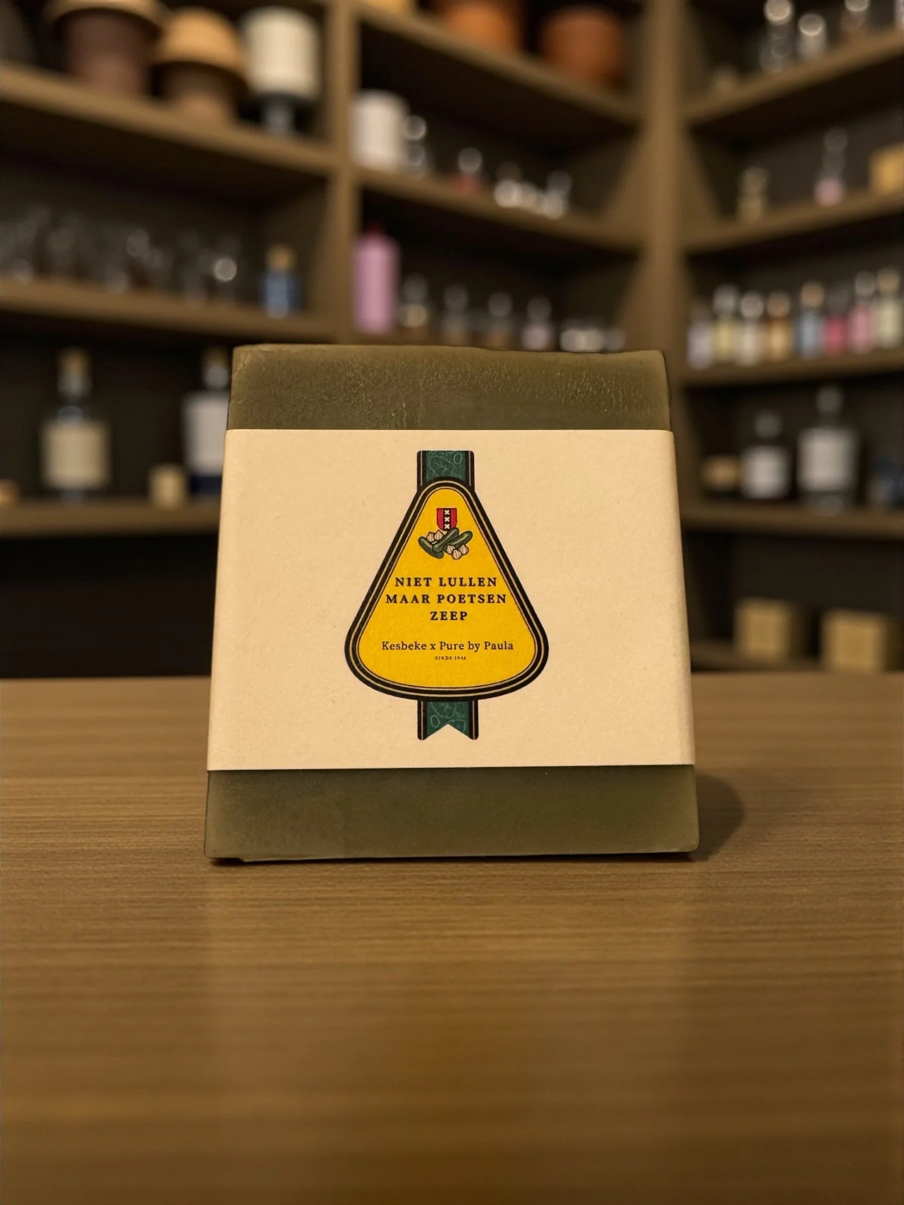 Box of soap with Dutch label, placed on a wooden surface with shelves of bottles in the background.
