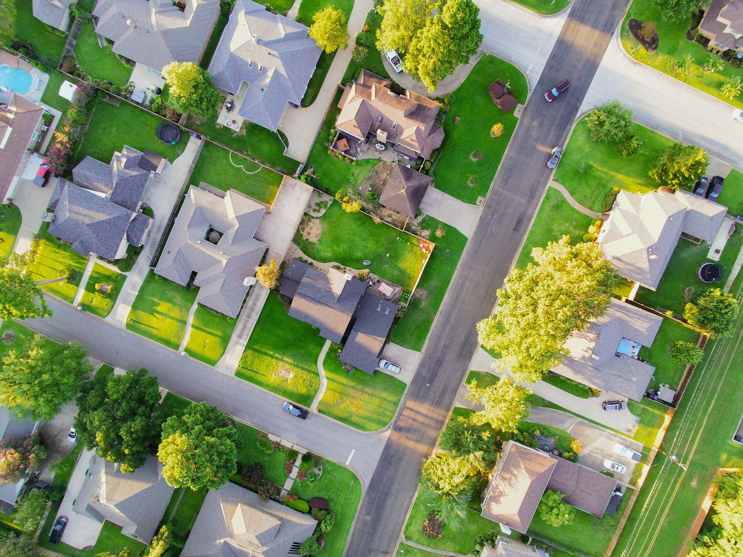 Aerial view of a suburban neighborhood with houses, green lawns, trees, and streets.
