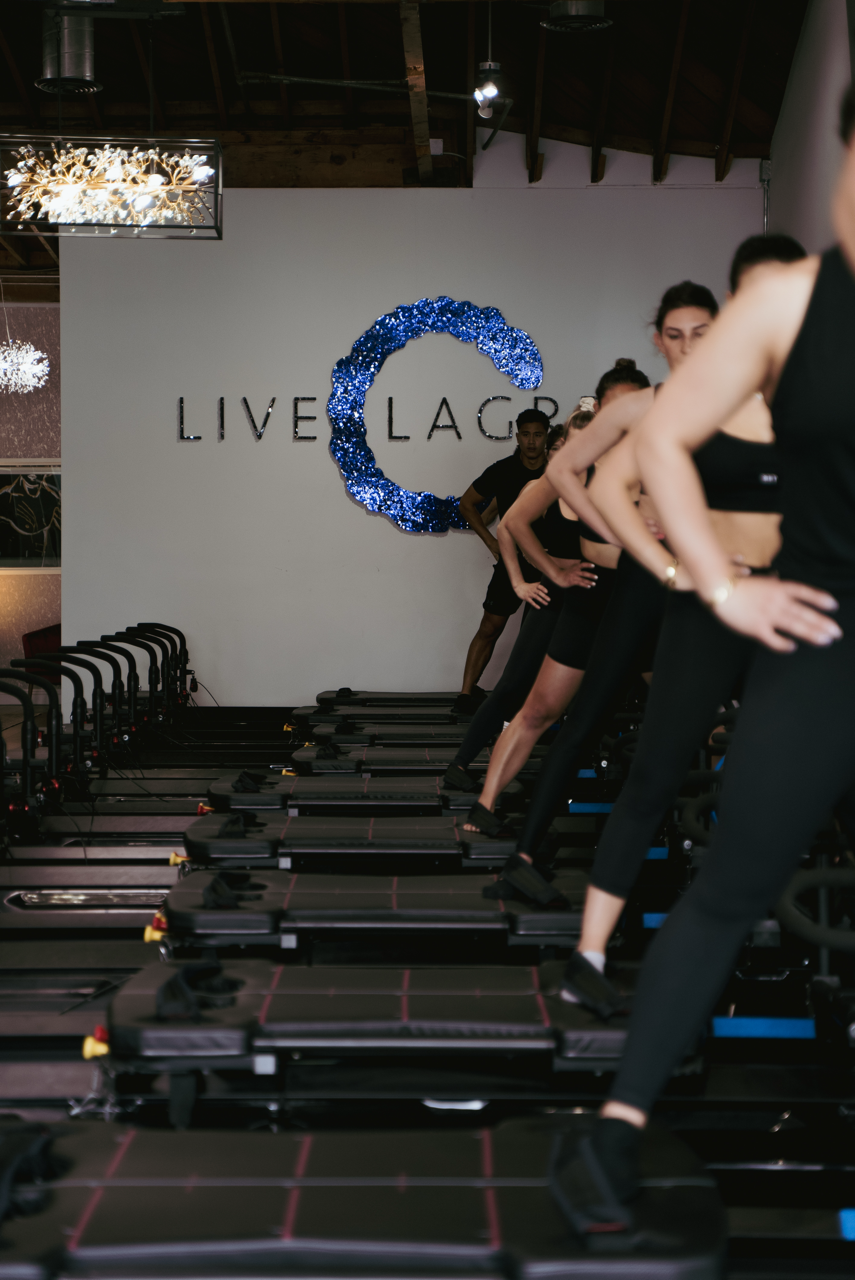 photo of 6 people standing on a pilates reformer with the LIVE LAGREE logo in the background