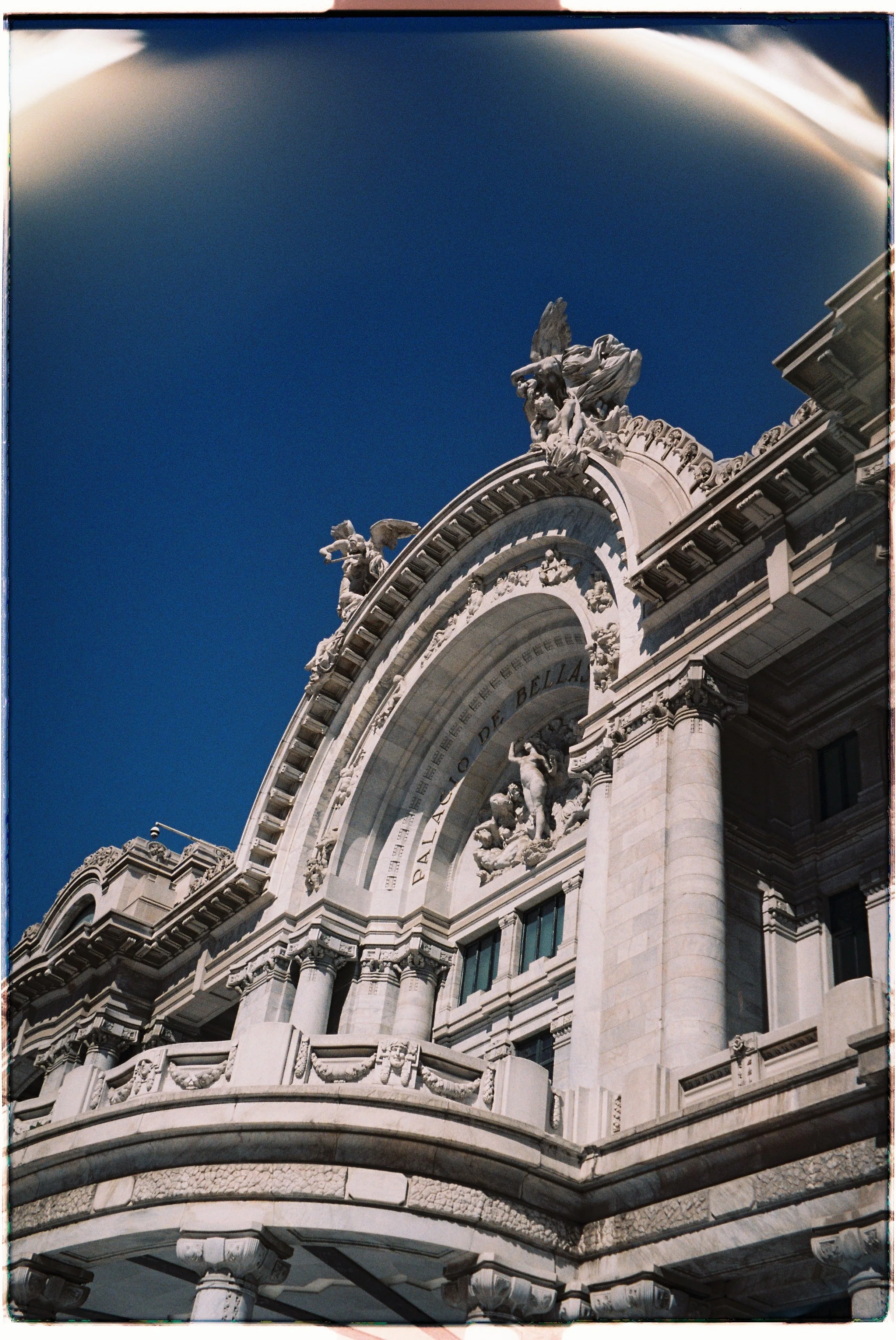 Close-up of ornate architectural details on a historic building, including sculptures, decorative cornices, and columns against a clear blue sky.