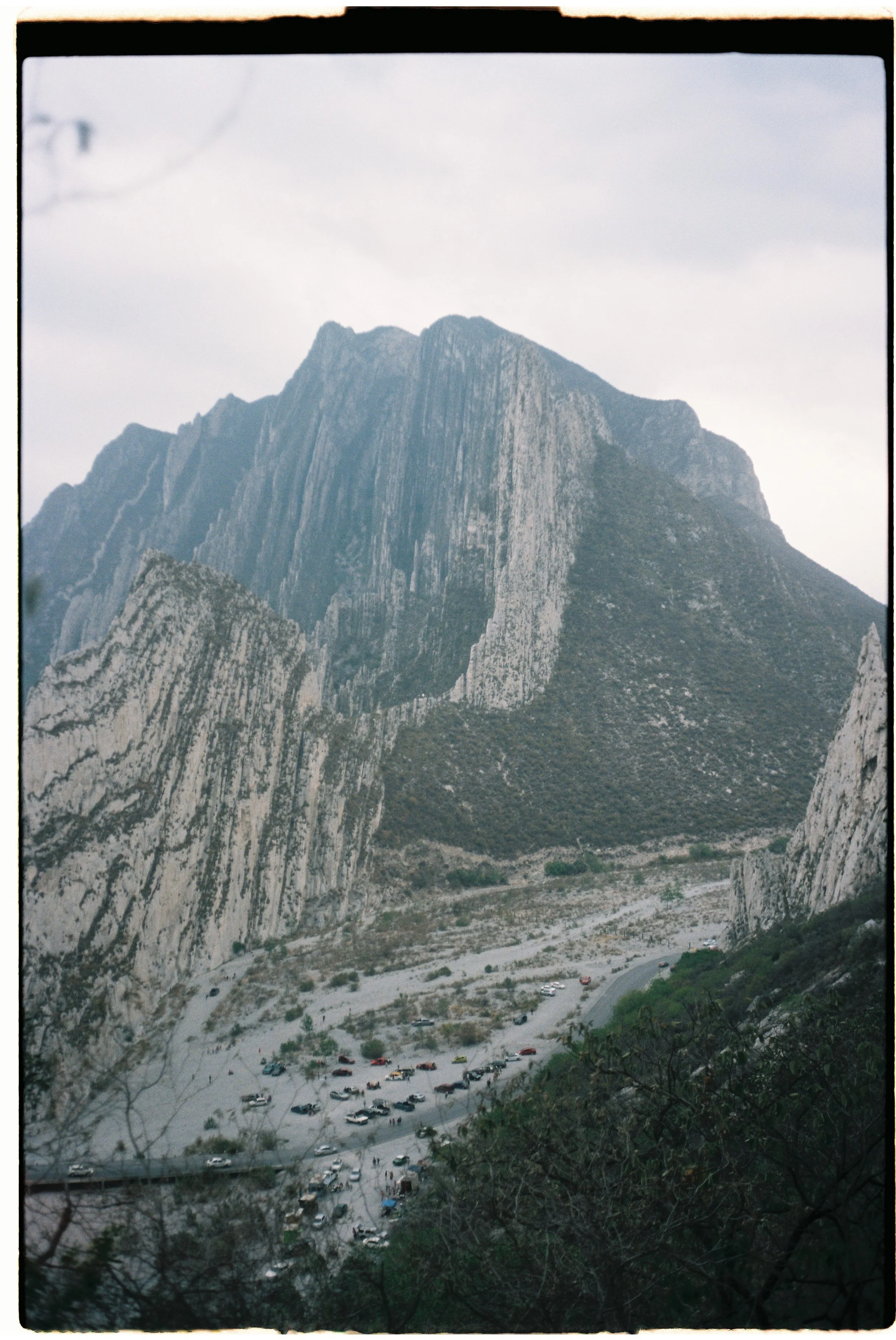 View of the Half Dome rock formation in Yosemite National Park with a parking lot and trees at the base, under an overcast sky.