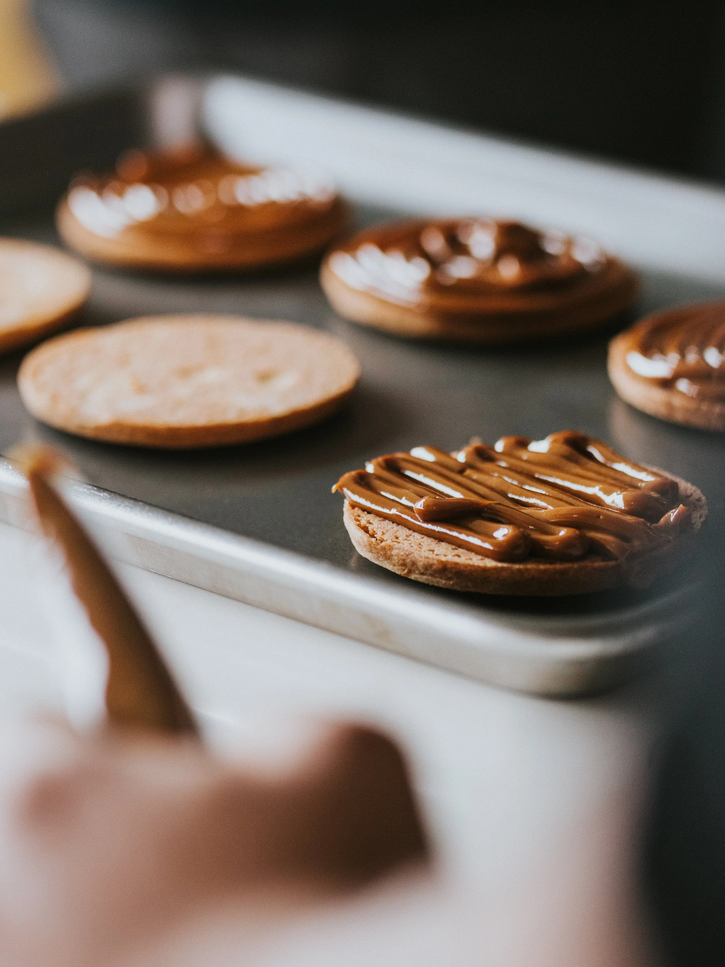 Close-up of assorted cookies and pastries with chocolate and caramel toppings on a baking sheet.