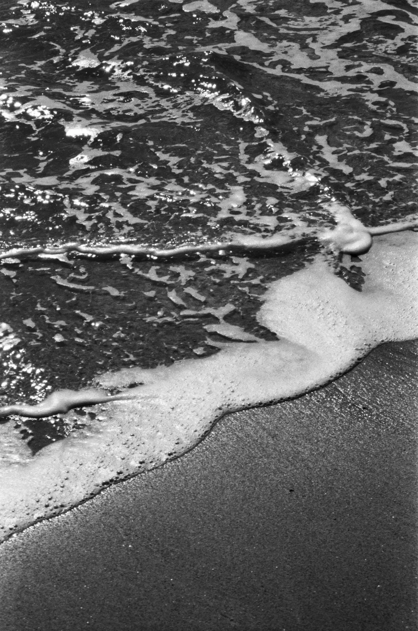 Black-and-white photo of waves gently washing onto a sandy beach.