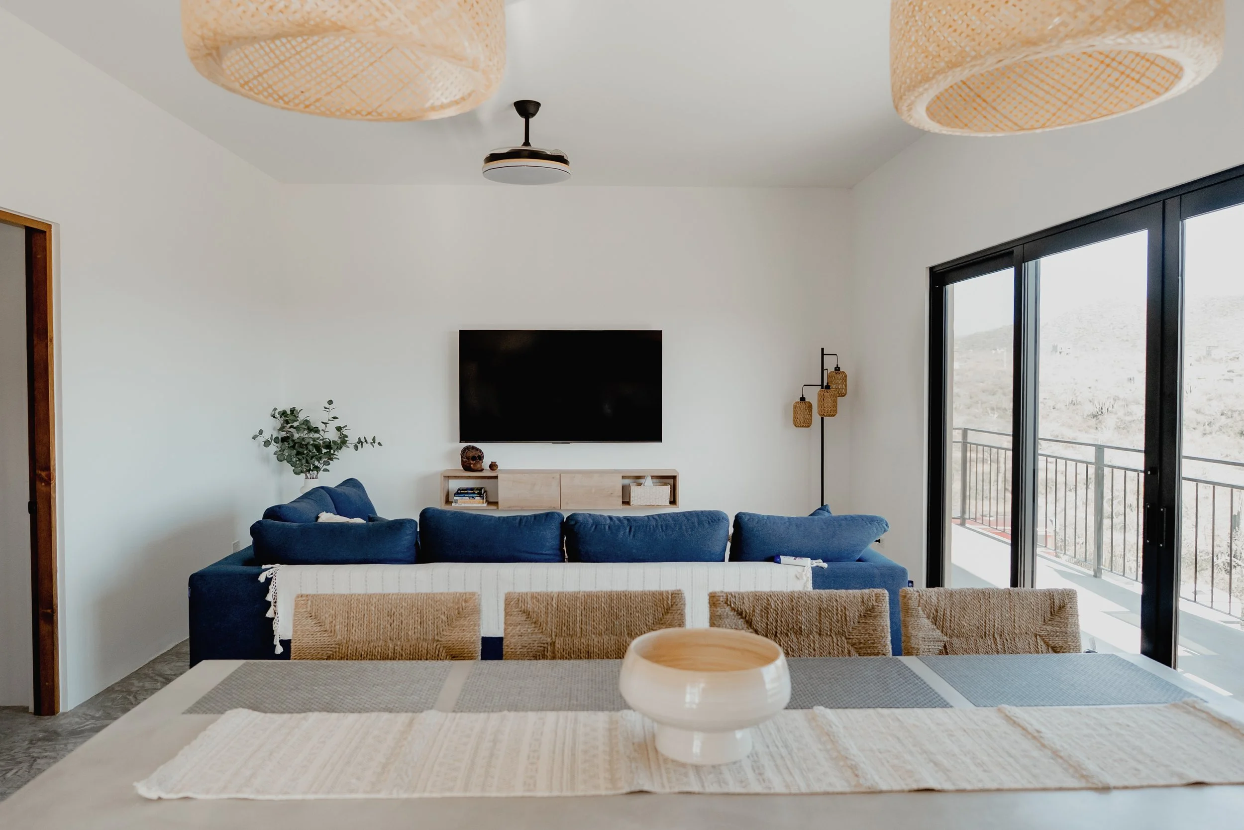Living room with white walls, a blue sofa, flat-screen TV on the wall, and large sliding glass doors with mountain views.