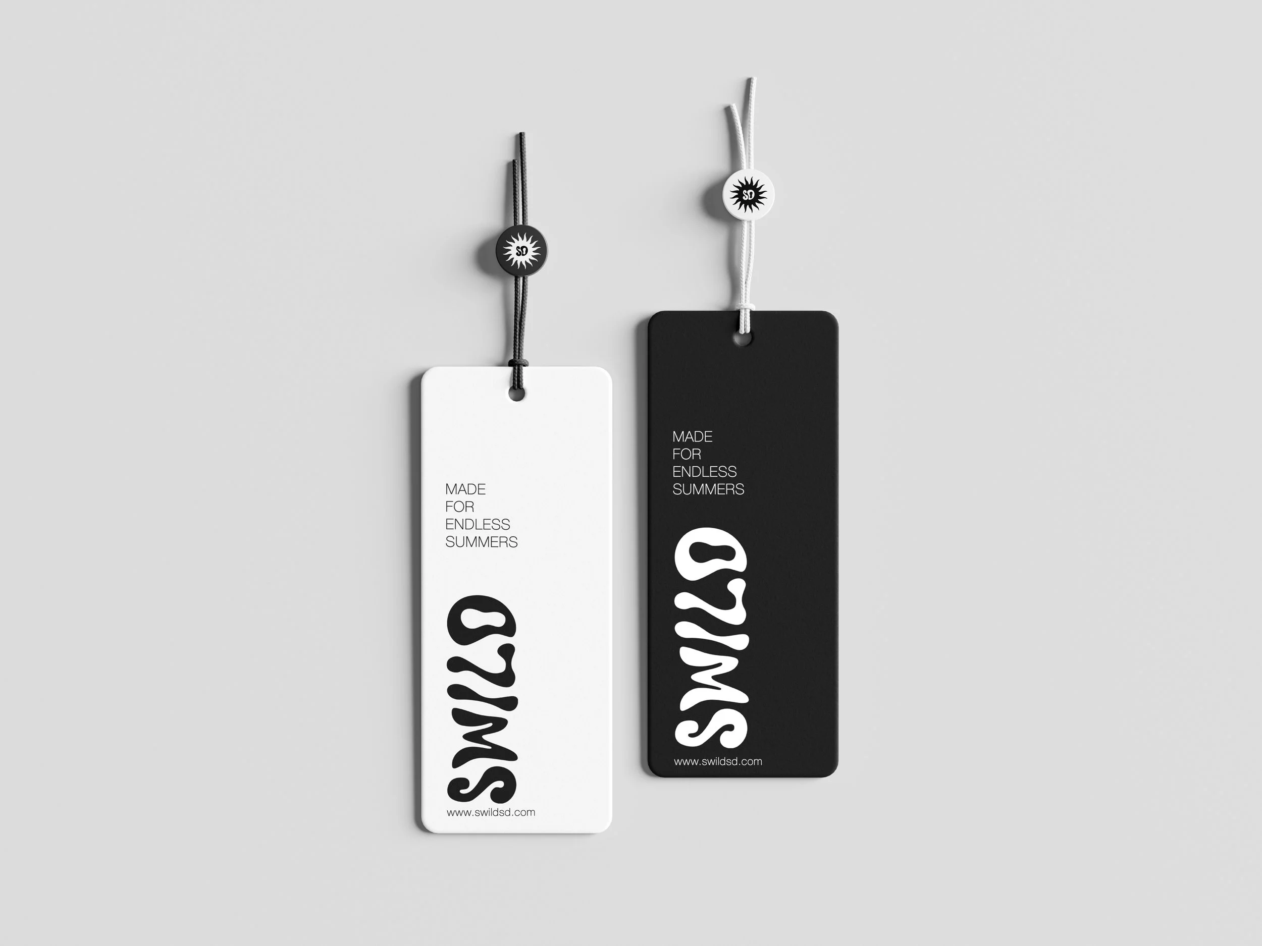 Two rectangular tags, one white and one black, hang on strings against a light gray background. The tags have the phrase "MADE FOR ENDLESS SUMMERS" and the website "www.swildsd.com" printed on them, with large stylized letters. The strings are tied t