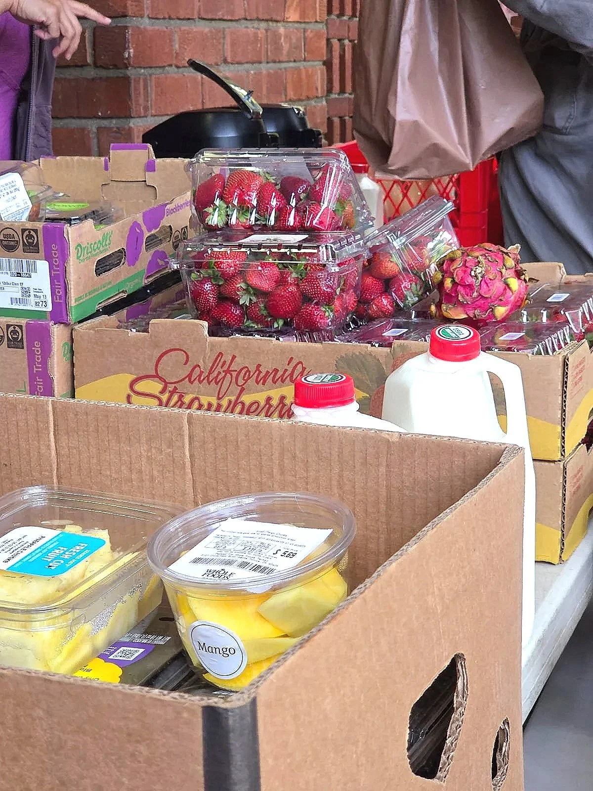 Box of fresh strawberries, a dragon fruit, and containers of sliced mango for sale at a market stand.