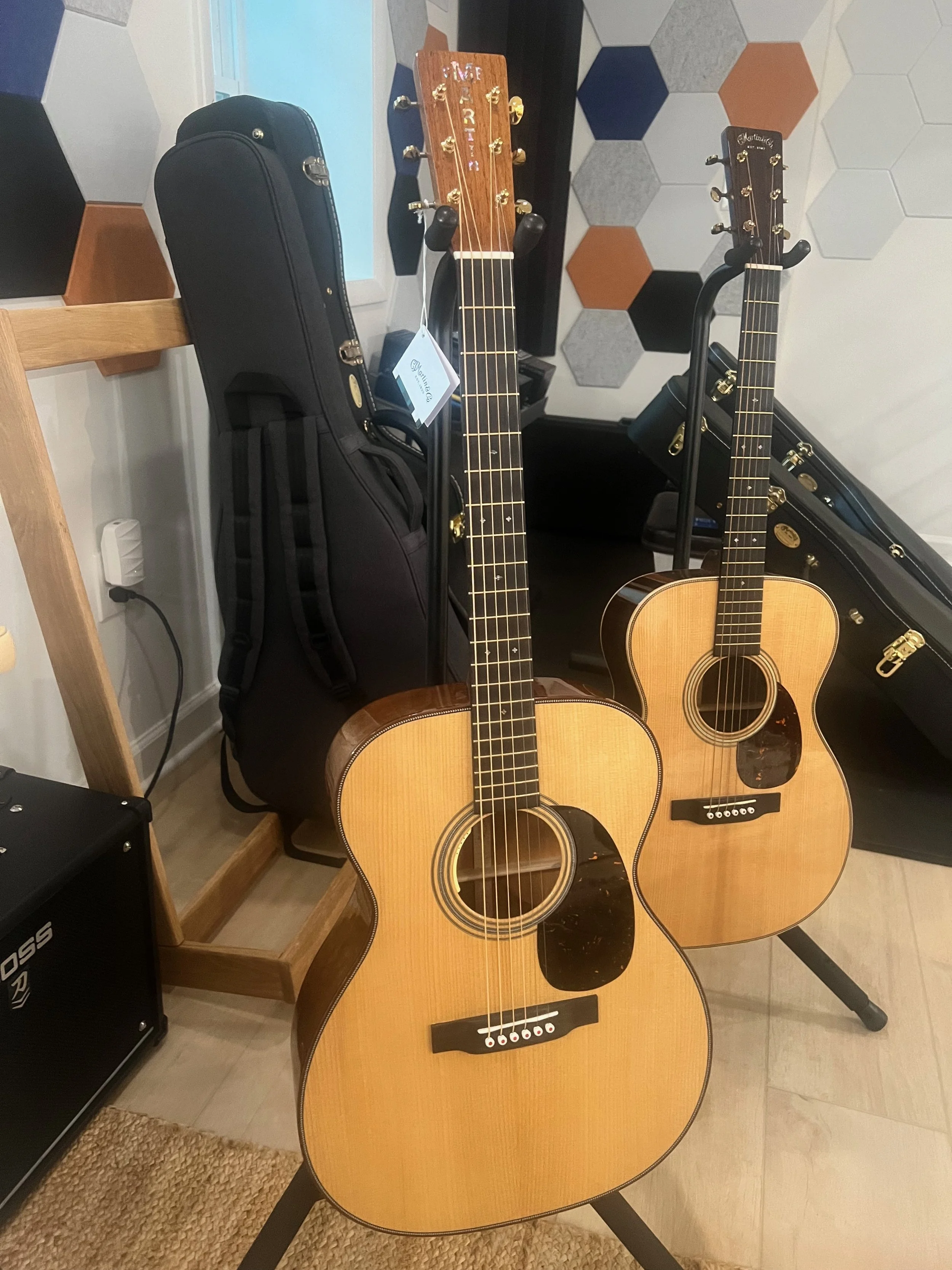 Two acoustic guitars in the foreground, with guitar cases and an amplifier in the background and to the side.