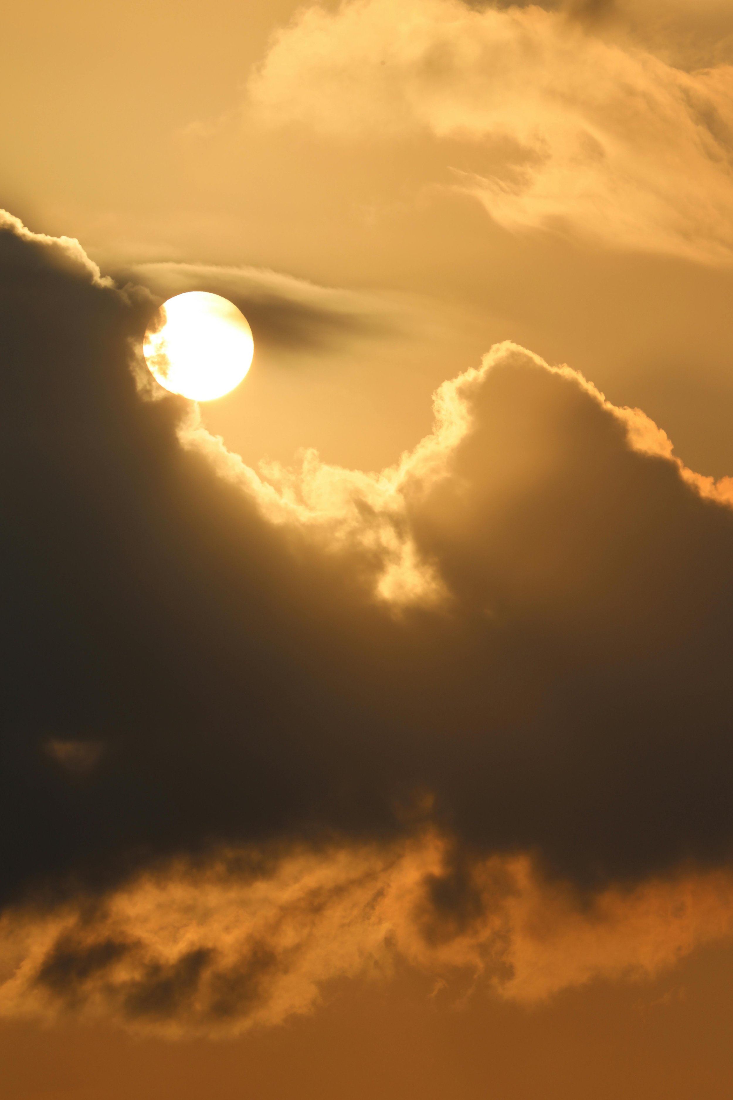 Sun partially covered by dark clouds during a sunset or sunrise, with golden and orange hues in the sky.