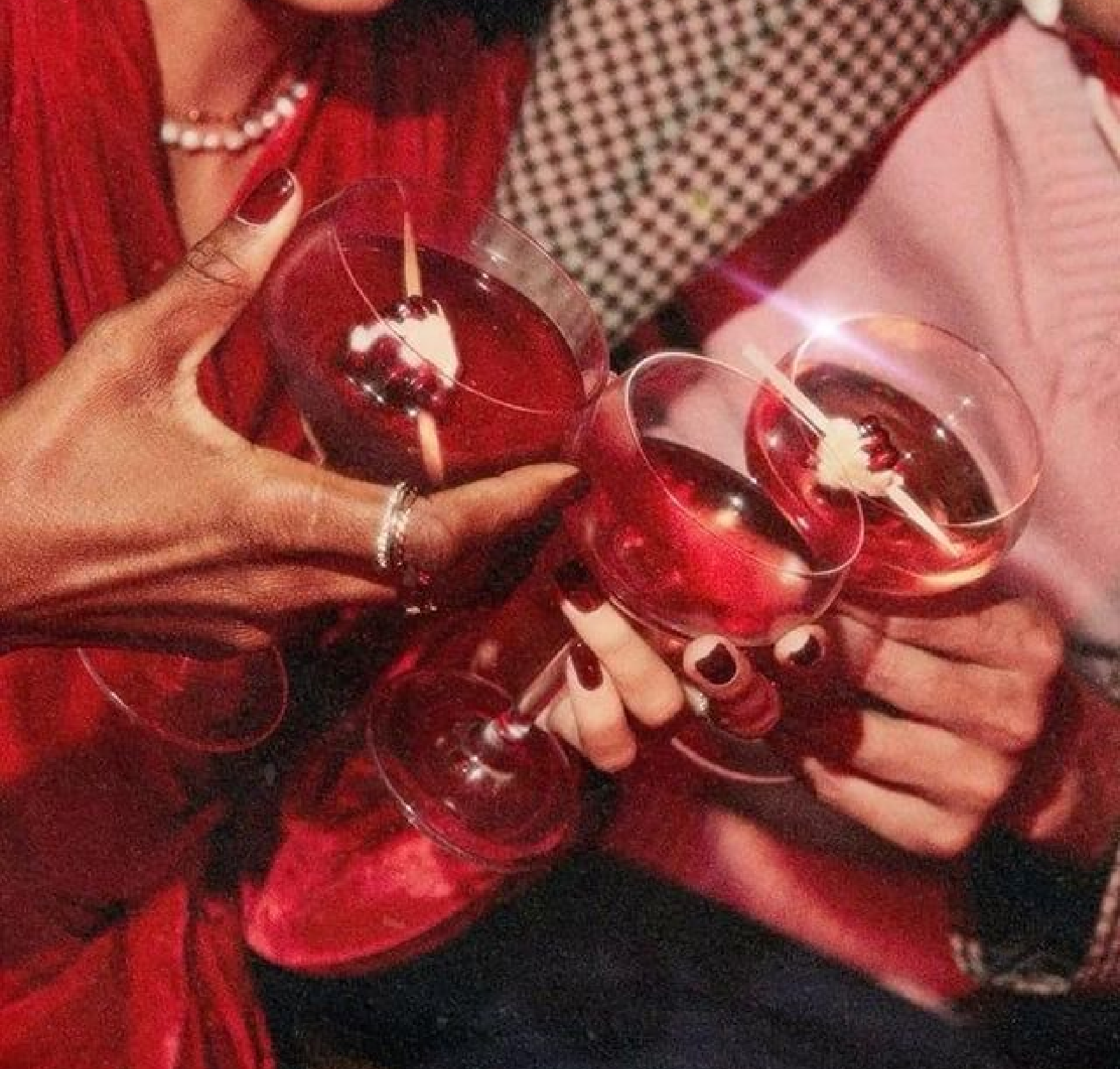 Multiple glasses of red wine held by people dressed in red and pink clothing, celebrating together.