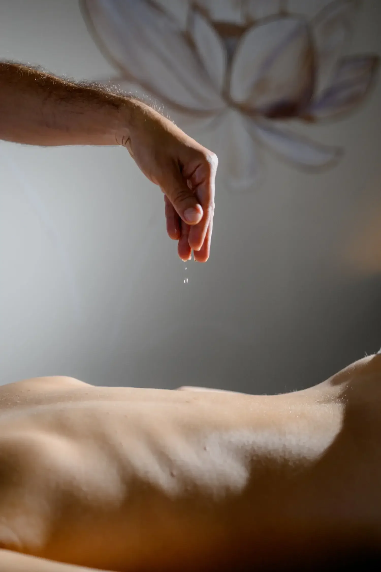 Close-up of a hand dripping water onto a person's bare back.