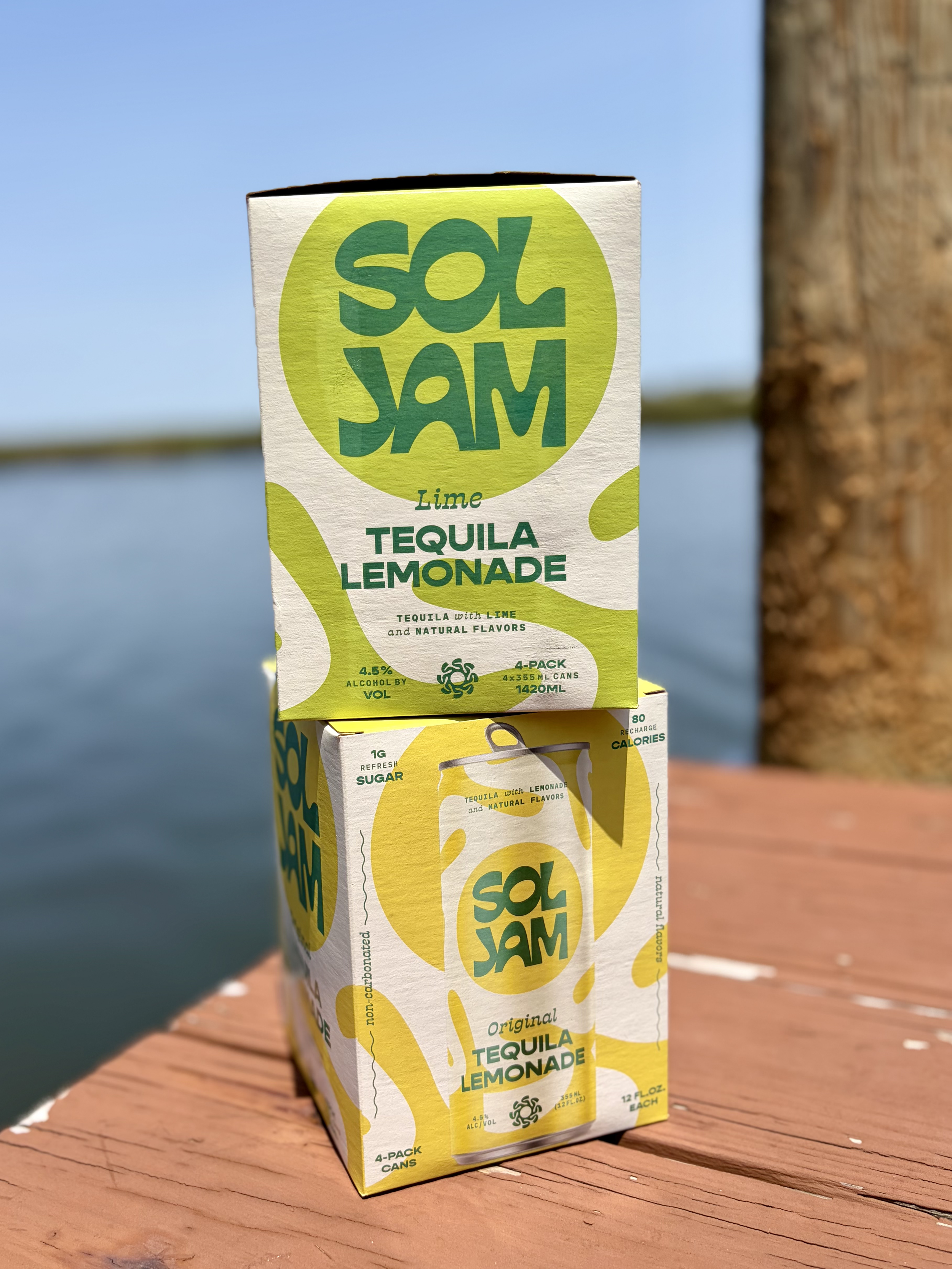 A Sol Jam Lime Tequila Lemonade carton on a wooden surface with a blue sky background.