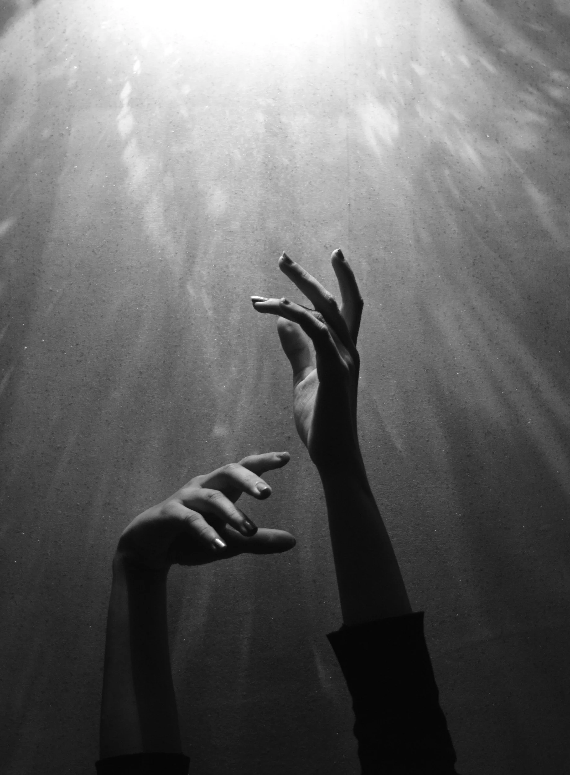 Hands reaching upward through dark water toward light at the surface.