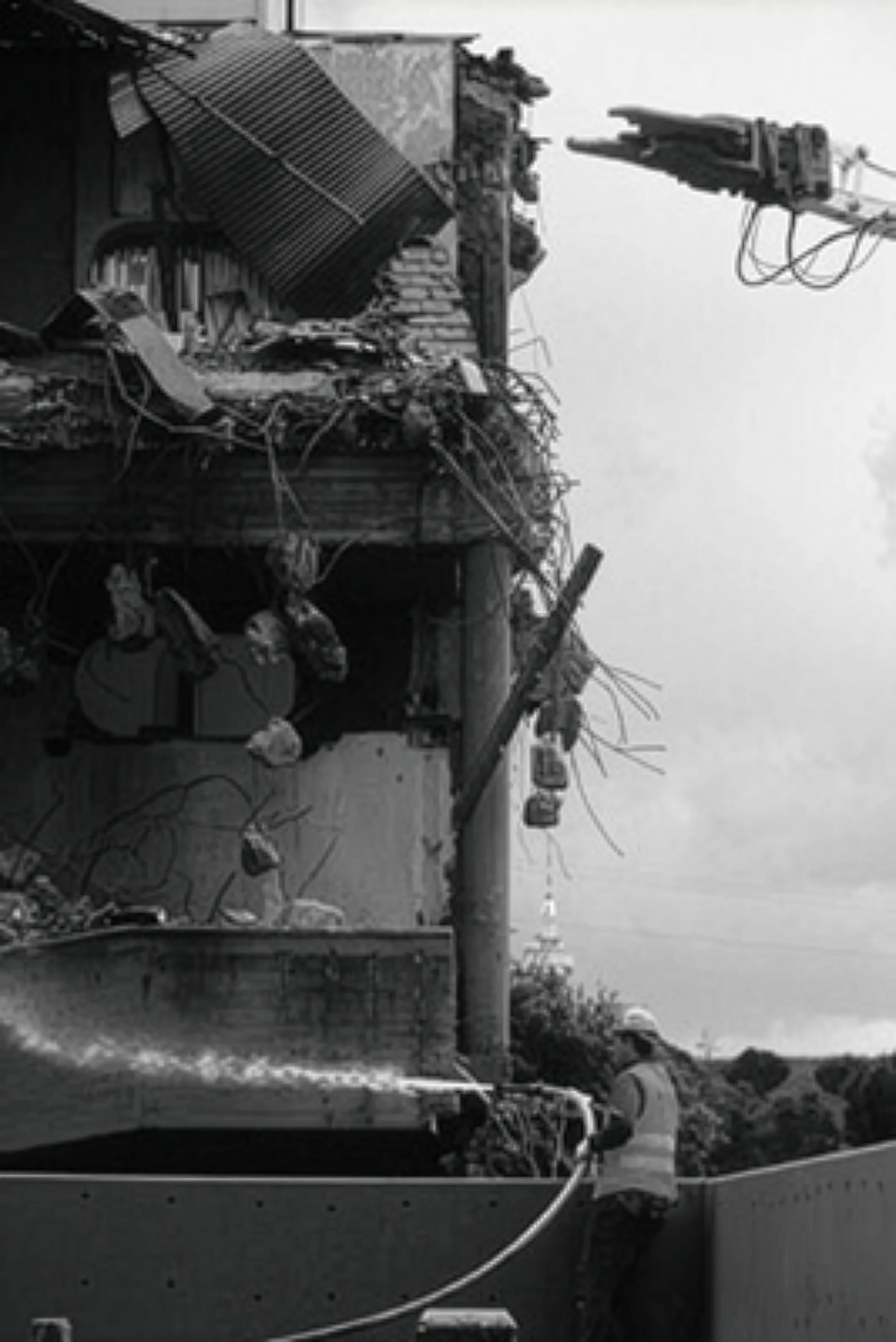 A person in a safety vest buoys a utility pole that has been damaged in an accident, with wires and debris hanging from the building's structure.