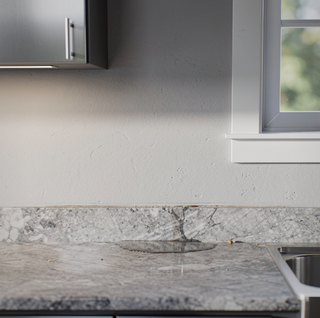 Kitchen counter with gray marble backsplash and window, white wall above, and cabinet with handle visible.