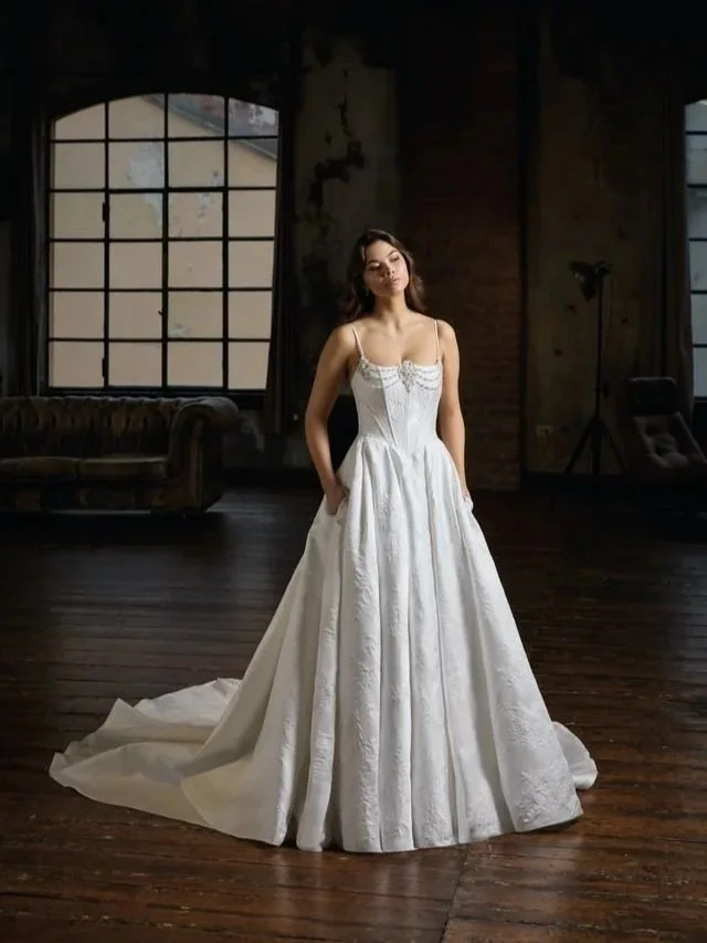 A young woman in a white lace wedding dress standing outdoors against a rocky background.
