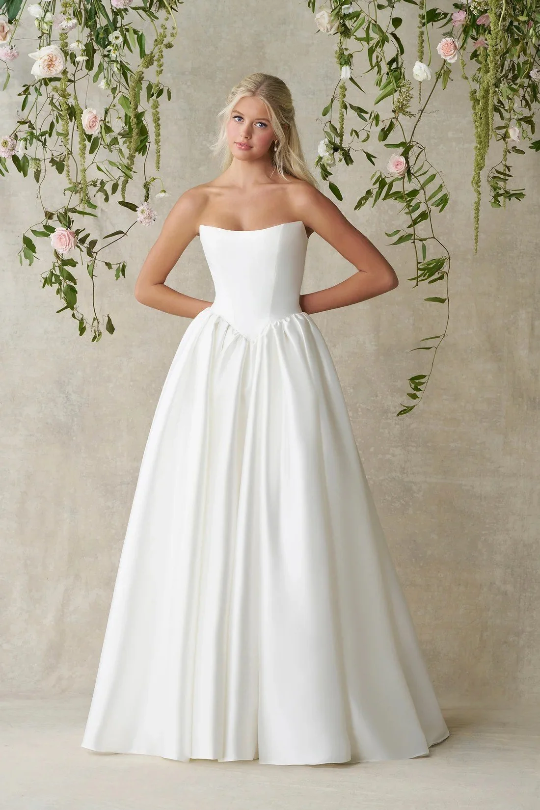 A woman in a strapless white wedding gown with a full skirt decorated with 3D floral appliques.