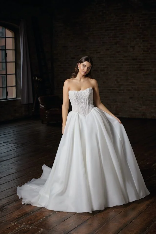 A woman in a strapless white wedding gown with a full skirt decorated with 3D floral appliques.