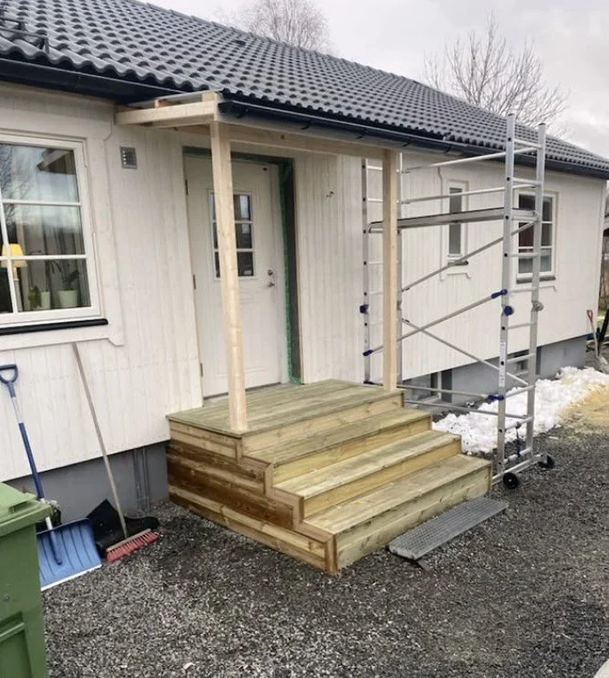 Byggarbetsplats vid ingång till ett hus med trätrappa och scaffolding.