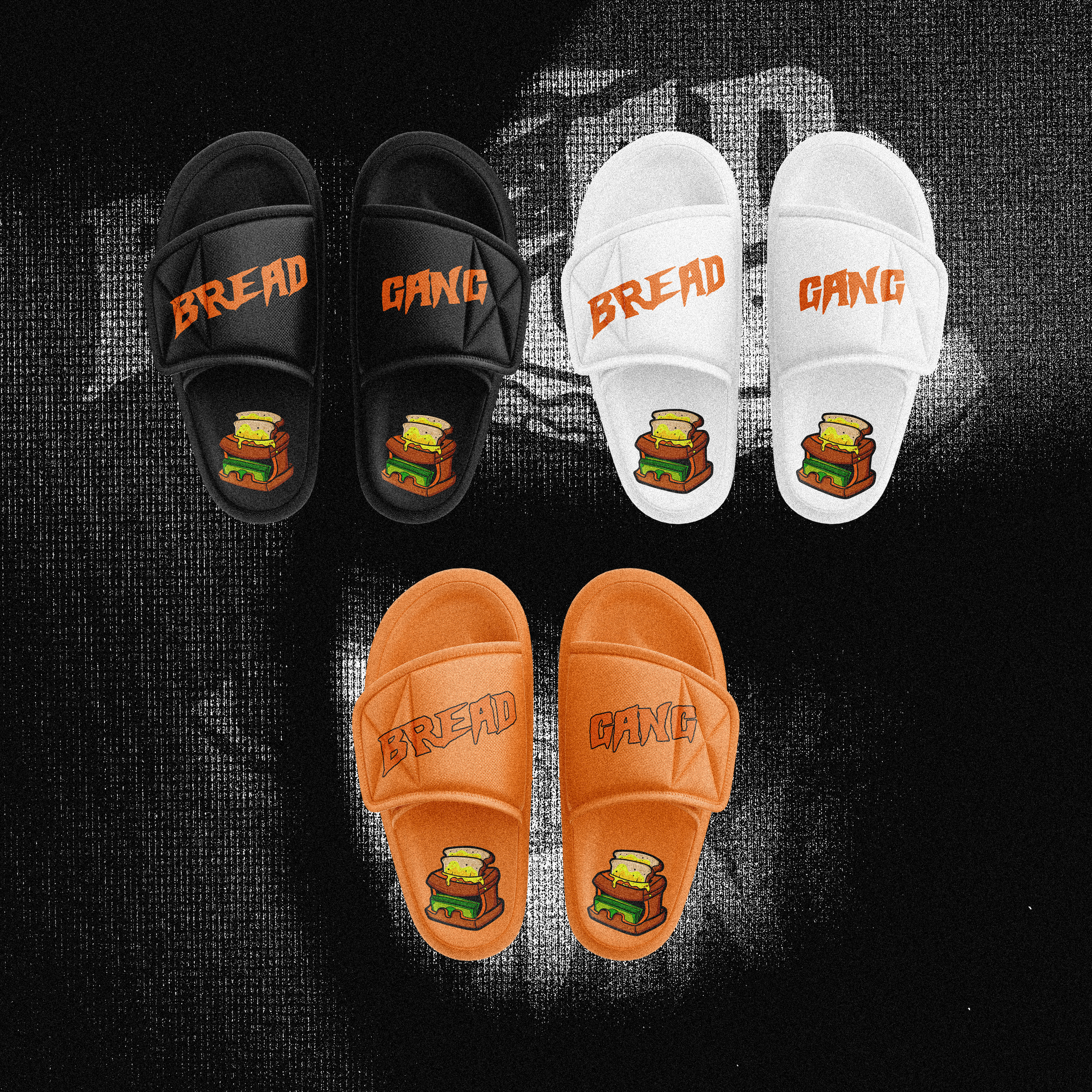 Three pairs of slides in black, white, and orange with the words 'Bread' and 'Gang' printed on the straps and a burger graphic on the foot area, placed on a textured black and white surface.