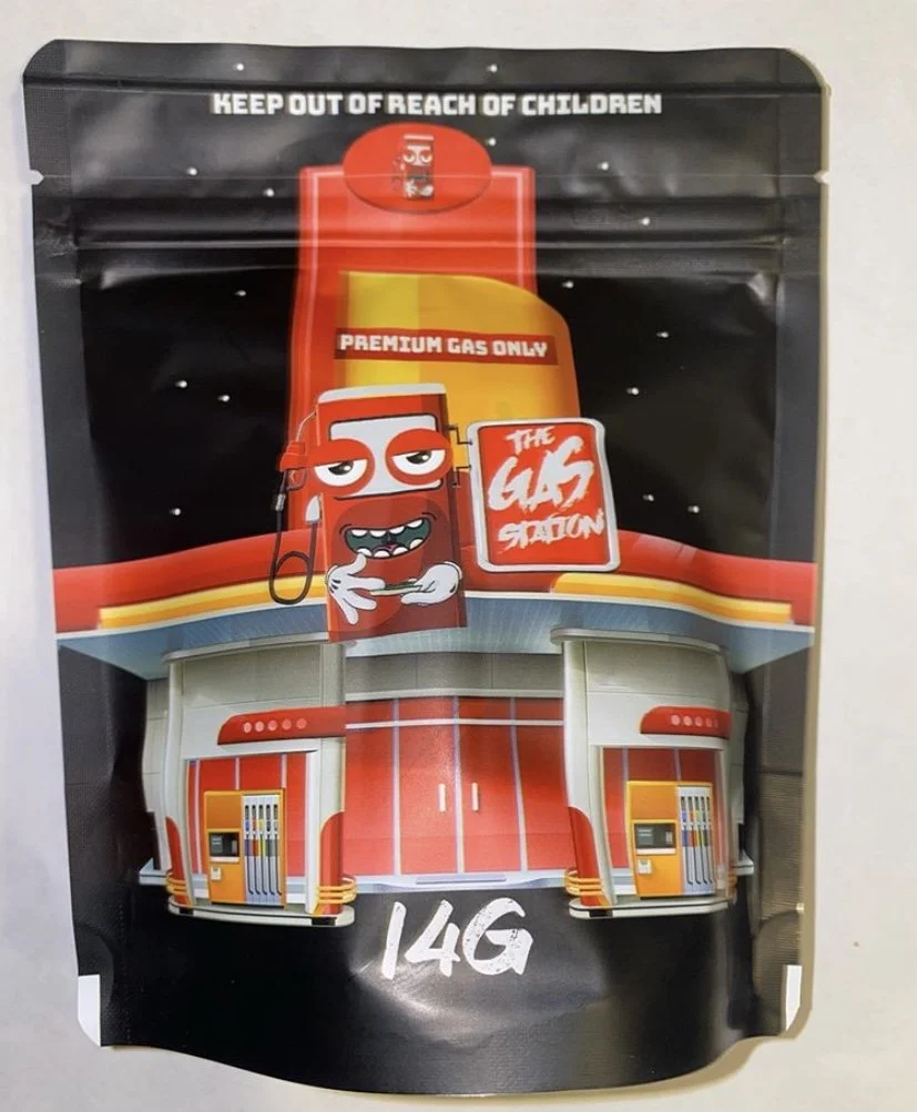 Packaging of a fuel can in a cartoon style with a red and yellow color scheme, featuring a animated red gas station character with a smiling face, holding a checkered flag, and the text 'The Gas Station' on a sign. The package indicates it is for pre