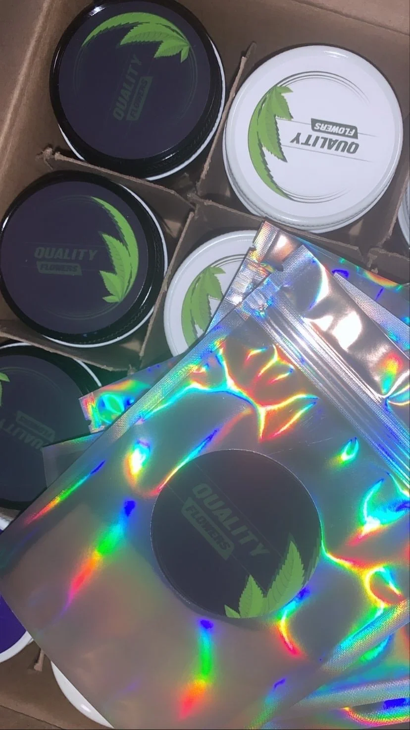 Multiple flat containers with green leaf graphics inside a cardboard box, some are covered with holographic wrapping.