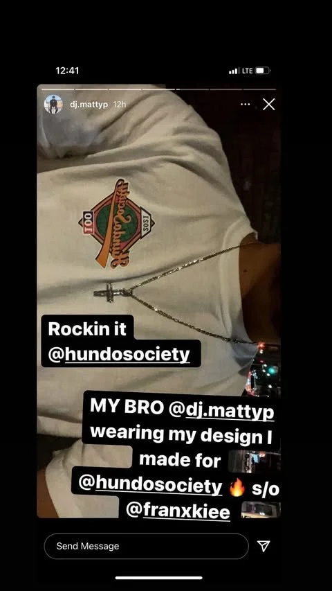 Close-up of a person wearing a white t-shirt with a logo, a silver chain with a cross pendant, and a caption about rocking it with a design created for Hundosociety, mentioning DJ Mattyp and Franxkie.