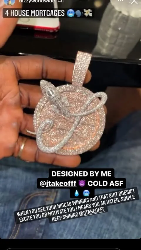 A hand holding a large, diamond-encrusted pendant in the shape of a dollar sign, attached to a chain. The pendant is decorated with numerous small diamonds.