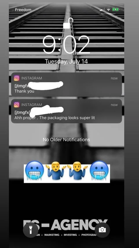 A smartphone lock screen showing the time 9:02, date Tuesday, July 14, with two Instagram message notifications, and animated emojis at the bottom of a blue face mask, people shrugging, and a blue face mask, on a background of train tracks. There is 