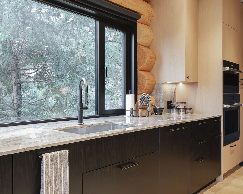 Kitchen sink under a window into the forest, black tap on a stone counter