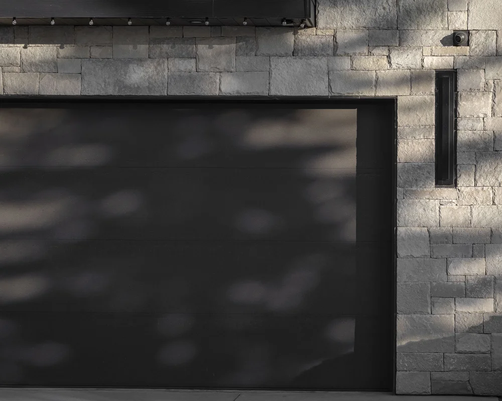 Dark garage door in a stone wall, branch shadows falling across both