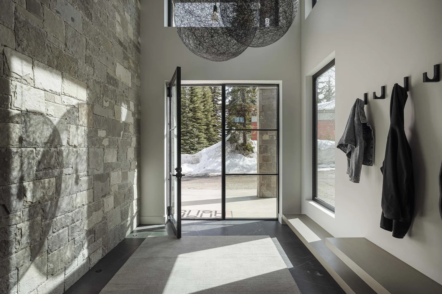 Entry hall with sun raking across a stone wall, glazed door open to snow