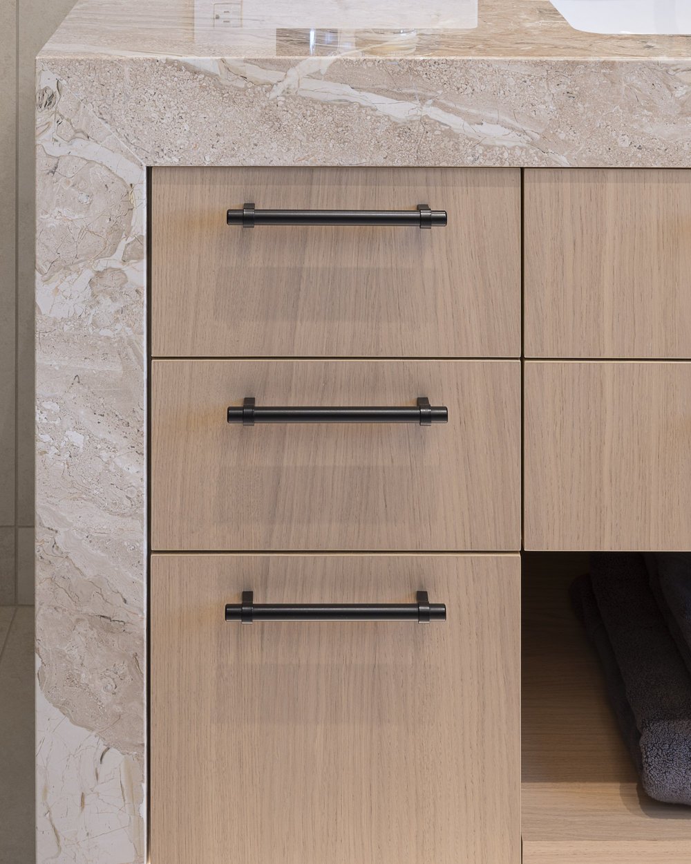 Close on pale wood drawers with black bar pulls, a stone slab at left