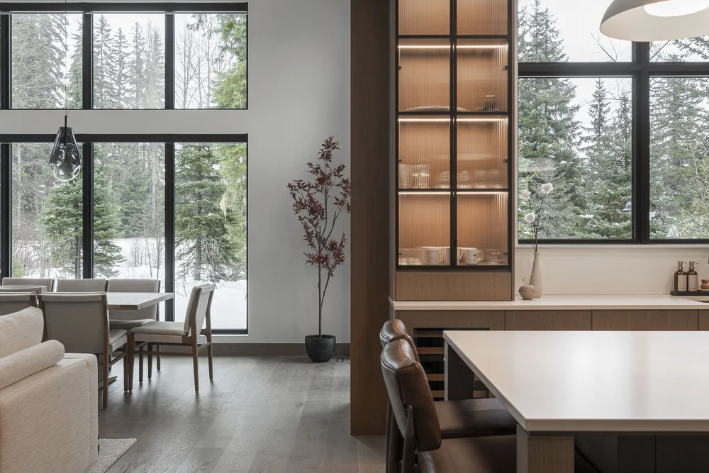 Living and dining seen past the island, lit display cabinet and windows onto snow