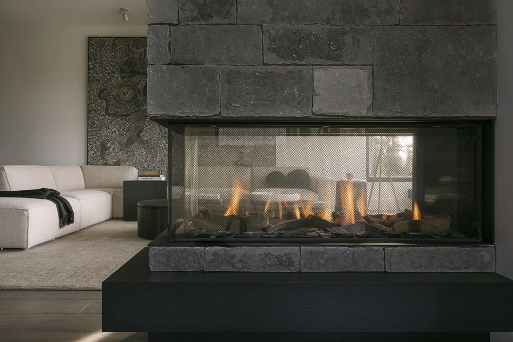 Living room with a stone fireplace alight and a pale sectional facing it
