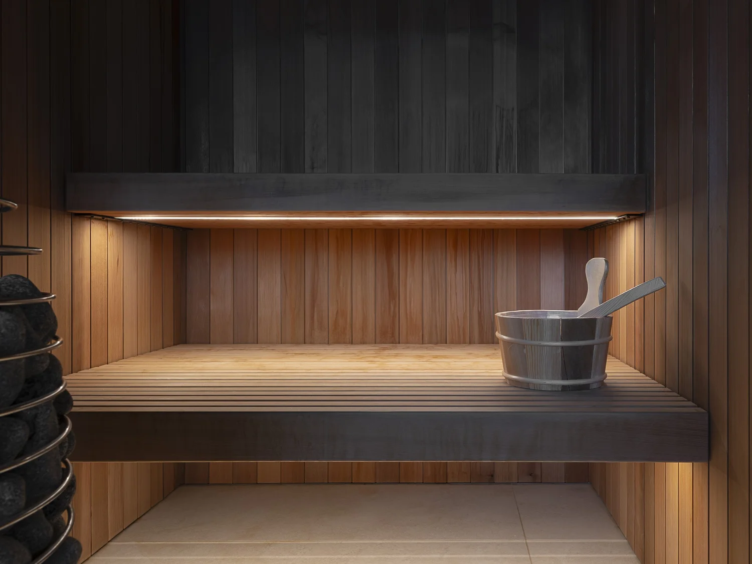 Sauna benches lit from beneath, a wooden bucket and ladle on the upper bench