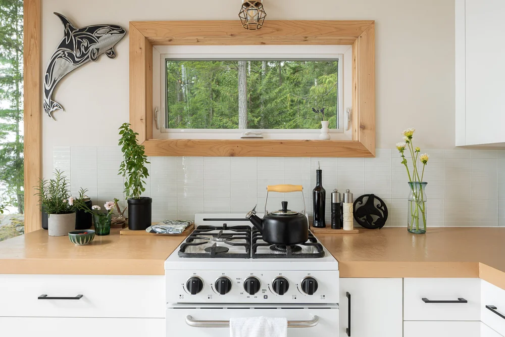 The range below a wood framed window, herbs and cut flowers along the counter