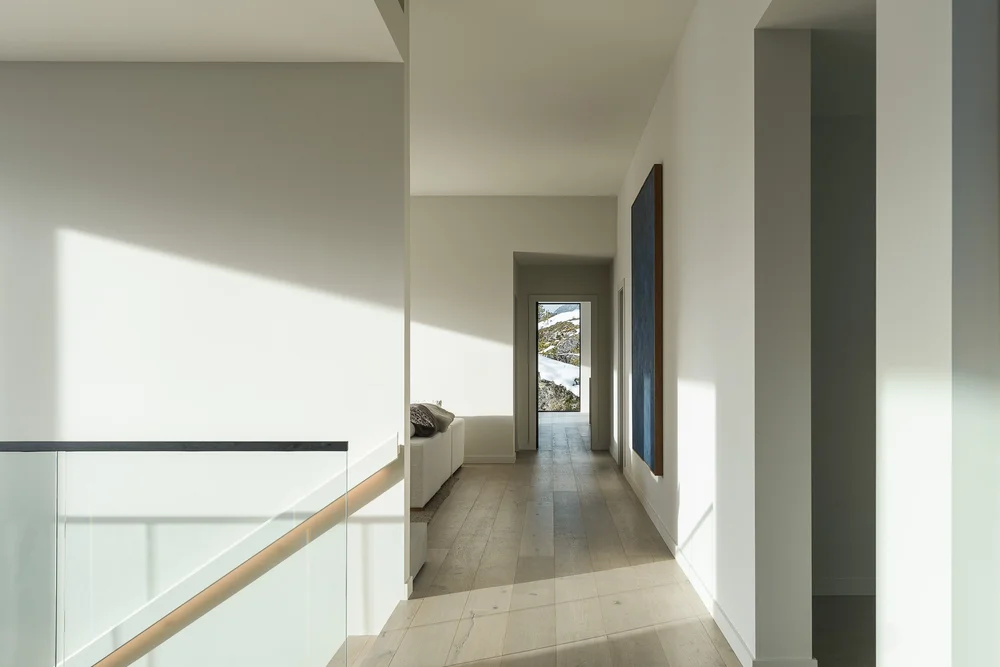 Upper hall in daylight, glass balustrade at left and a framed work at the end