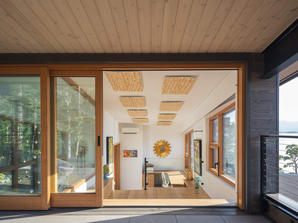 Office through a wide sliding door, framed art and woven ceiling panels beyond