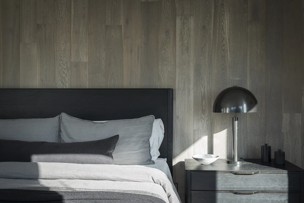 Bed against a wood panelled wall, a domed lamp on the nightstand in sun