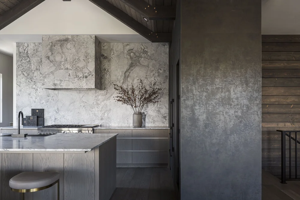 Kitchen beside a tall dark panel, stone counters and a stool at the island end