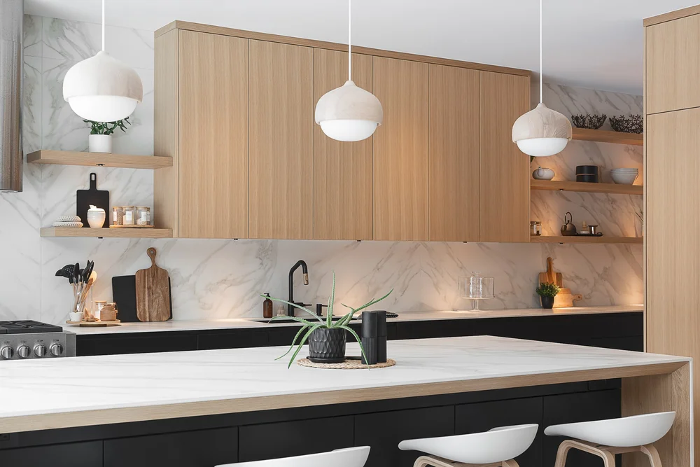 Kitchen island under three globe pendants, pale timber cabinetry above dark lower units