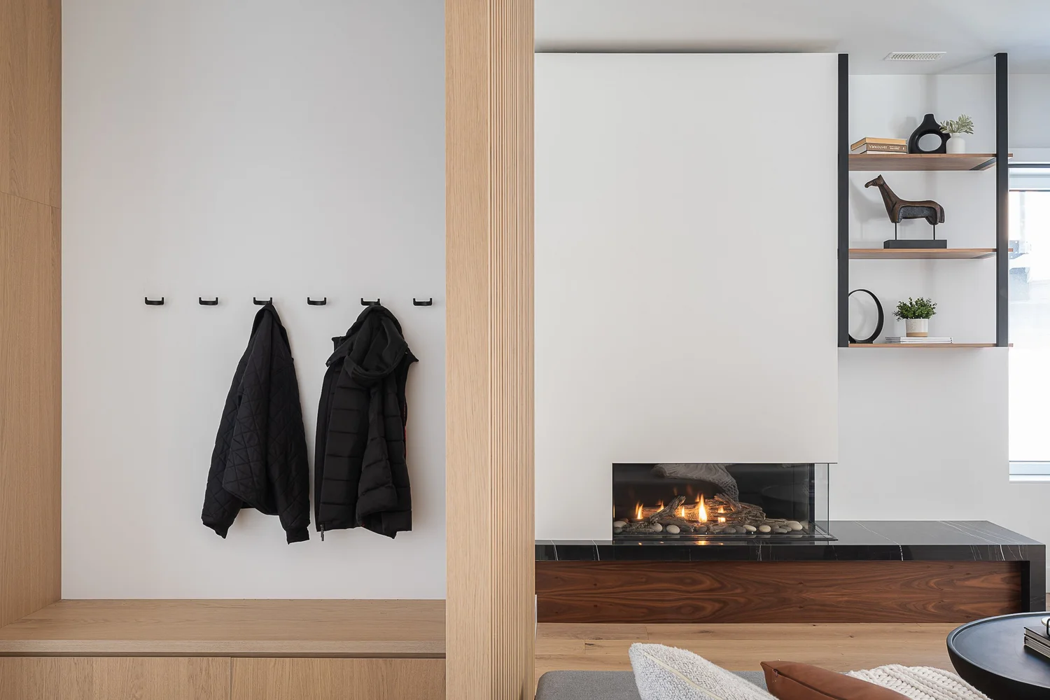 Entry bench and black wall hooks holding two dark coats, a lit fireplace beyond