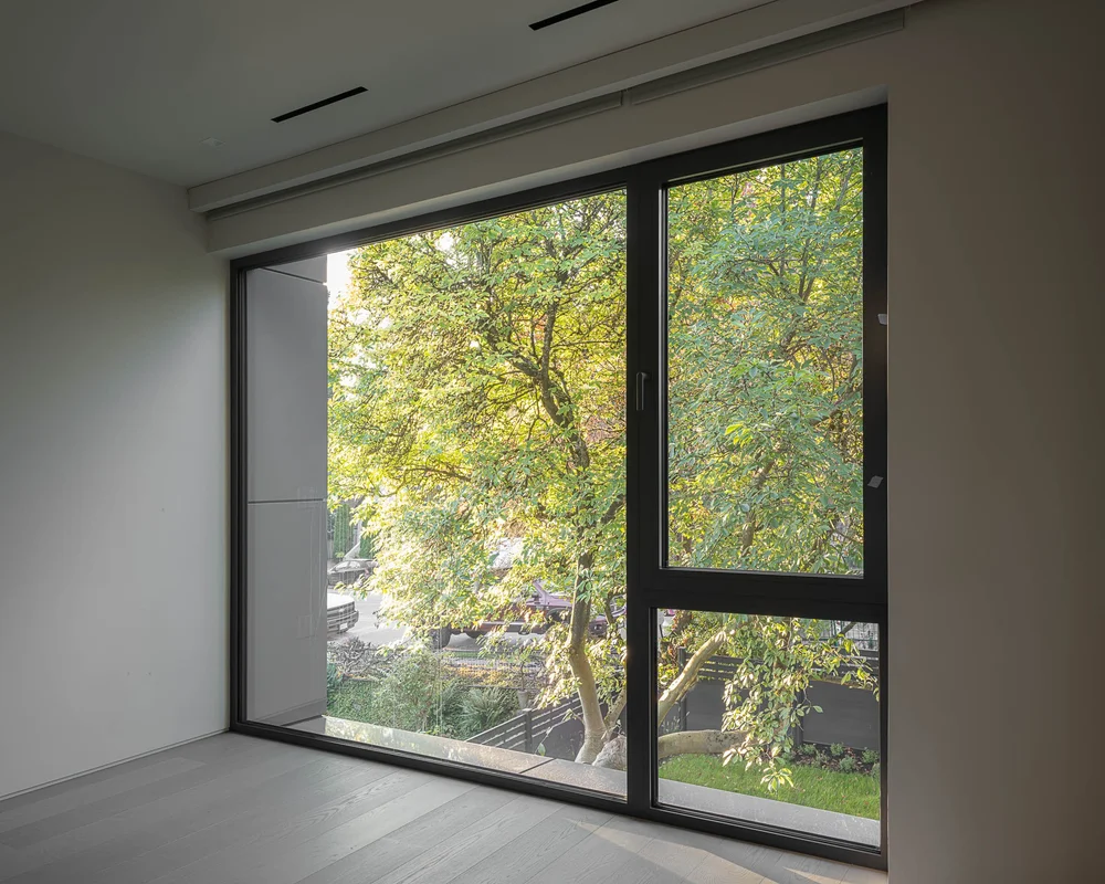 A large corner window filled with one broad tree, plank floor and bare walls