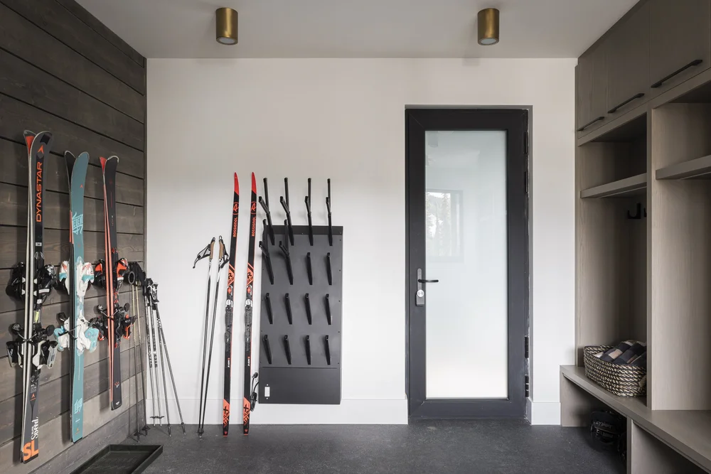 Mudroom with skis and poles on a wood wall, boot rack and glazed door