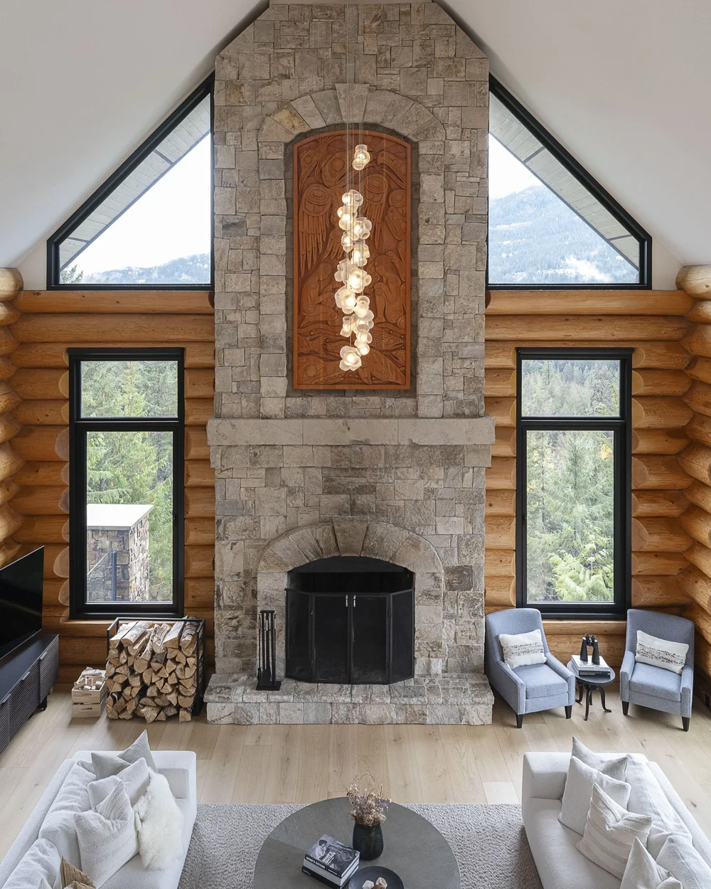 The stone chimney rising the full height of the room, a cascading light fixture in front