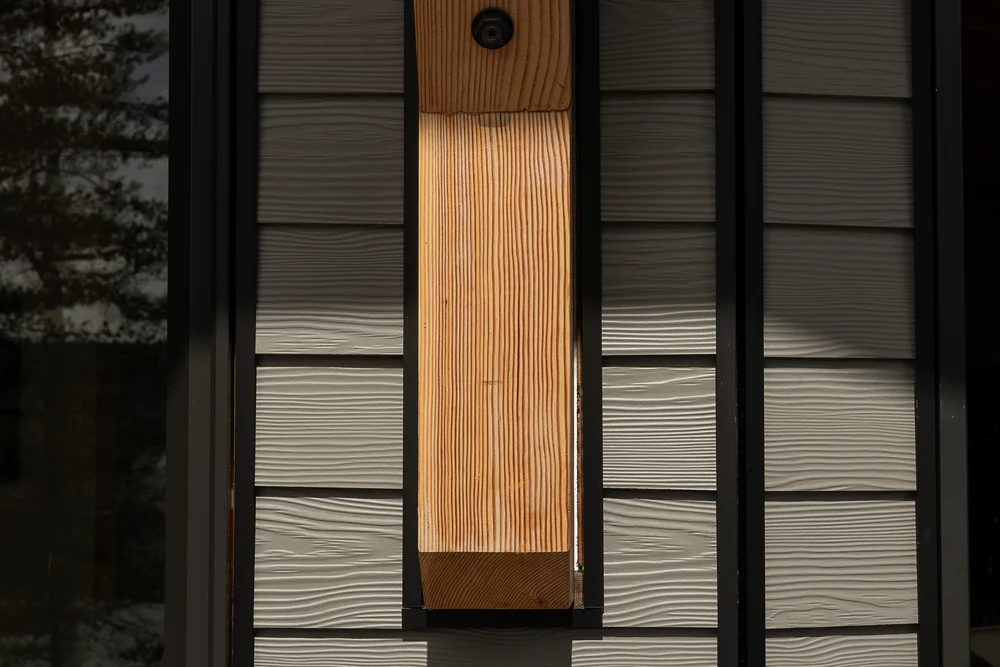 A wide wood post set between dark window frames and textured lap siding